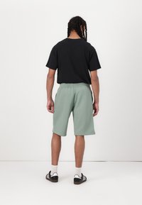 Μαύρο κοντομάνικο μπλουζάκι συνδυασμένο με ανοιχτοπράσινα σορτς με ελαστική μέση. Τα σορτς έχουν χαλαρή εφαρμογή και πλάγιες τσέπες. Μαύρα αθλητικά παπούτσια με λευκές κάλτσες.