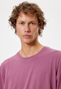 T-shirt girocollo viola chiaro in cotone. Design semplice con maniche corte e una texture liscia e uniforme. Senza fantasie o accenti visibili.