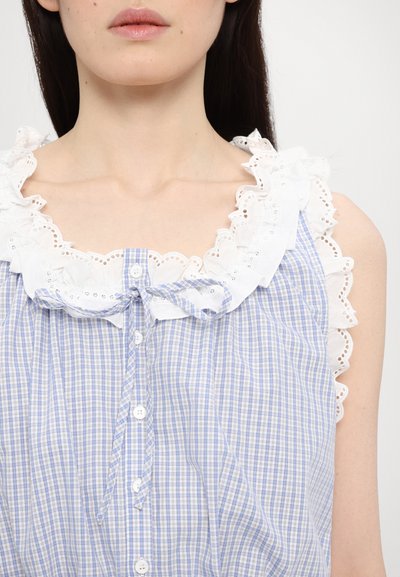Blauw-witte geruite top met een gegolfde witte franje halslijn, met een knopenfront en een strikdetail bij de hals.