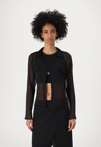 Veste noire transparente à manches longues avec un col, des poches avant et une conception ouverte, associée à un top et une jupe noirs.
