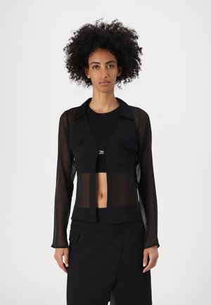 Schwarze, durchscheinende Langarmjacke mit einem kragenlosen Ausschnitt, vorderen Taschen und offenem Design, kombiniert mit einem schwarzen Oberteil und Rock.