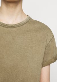 Khaki t-shirt z krótkim rękawem, okrągłym dekoltem i podwiniętymi rękawami. Tkanina ma miękką teksturę o delikatnym, jednolitym kolorze.