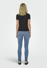 Svart kortärmad t-shirt, åtsittande design, ihopparad med ljusblå skinny jeans och svarta sneakers med vita accenter. Bakvy visas.