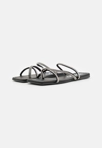 Sandale plate negre cu multiple curele subțiri, având accente metalice și un design al tălpii dreptunghiulare. Detaliu cu textură pe tălpicul pentru picior.