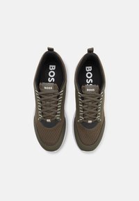 Baskets vert olive avec une tige en mesh texturée, une semelle en caoutchouc blanche, une doublure intérieure noire contrastante et des lacets ton sur ton avec un logo sur la languette.