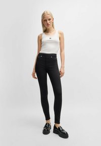 Jeans neri aderenti a vita alta, con accessori in metallo argentato e una consistenza liscia. Abbinati a un top bianco senza maniche e scarpe con plateau nere.