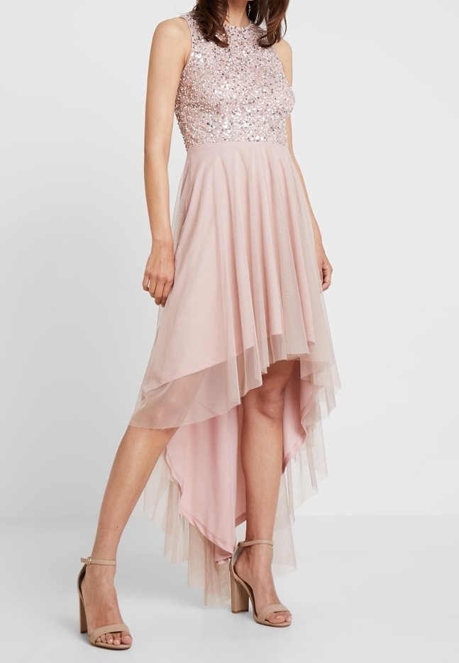 Jasnoróżowa sukienka z koralikowym, bezrękawnikowym gorsetem oraz warstwową spódnicą o kroju wysokim z przodu, niskim z tyłu. Materiał to miękki tiul o przezroczystej, lekko opadającej fakturze. Buty są w kolorze brązowym.