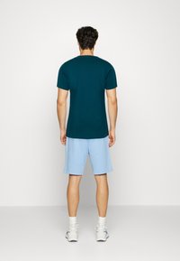 Tmavě modré bavlněné tričko s krátkým rukávem, doplněné o světle modré šortky. Oblečení doplňují bílé tenisky a ponožky do půli lýtek.