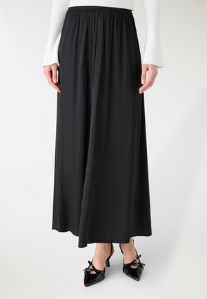 Maxi gonna nera e fluente realizzata in tessuto leggero, con vita elastica. Abbinata a scarpe nere in vernice con fiocchi.