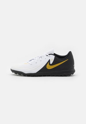 Crampon de football blanc et noir avec un swoosh doré Nike et une semelle en caoutchouc noire avec de petits crampons, vue de côté sur fond uni.