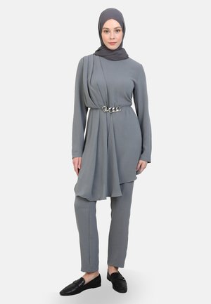 Conjunto de dos piezas gris que incluye una túnica de manga larga con detalles drapeados, un cinturón de cadena plateada y pantalones ajustados. Estilizado con un hijab a juego.