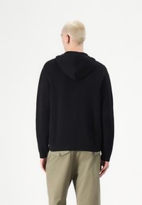 Svart hoodie i mjukt tyg med avslappnad passform och minimalistisk design, kombinerad med ljusa khakibyxor.