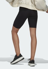 Svart ribbad cykelshorts med en åtsittande passform, kombinerade med svarta sportskor med en tjock vit sula. Bakgrunden är ljus och neutral.