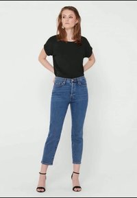 T-shirt preta de mangas curtas, combinada com jeans azuis de cintura alta, ajustados, até ao tornozelo, e sapatilhas pretas de tiras.