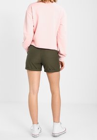 Pink cropped sweatshirt paired with dark green shorts. White high-top sneakers visible at the feet. Focus on casual, comfortable attire.
