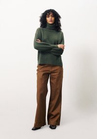 Groene gebreide coltrui met wijde mouwen en een geribbelde zoom, gecombineerd met bruine wijde corduroy broek en zwarte hakken.