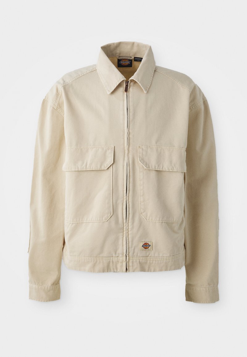 Veste beige légère avec fermeture éclair sur le devant, deux poches poitrine et un petit logo à l'ourlet. Fabriquée en tissu coton durable.