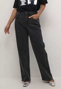 Jeans negros de tiro alto con corte recto, con una sutil textura de brillo. Combinados con bailarinas plateadas y una camiseta gráfica negra.