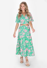 Completo floreale verde composto da un top corto con maniche ampie e una gonna maxi con orlo a strati, accentuata da fiori rosa.