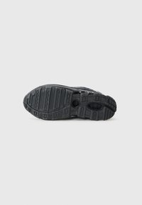 Black sneaker outsole with textured rubber, deep grooves for grip, circular accents, and unique tread patterns for traction.