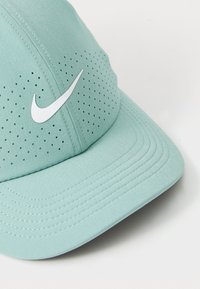 Lysgrøn cap lavet af tekstureret stof med ventilationshuller, prydet med et hvidt Nike swoosh-logo på forsiden og syede sømme.