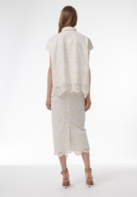 Vestido de encaje blanco con mangas cortas, dobladillo en forma de ondas y patrones florales. Silueta ajustada con textura intrincada en toda la prenda.