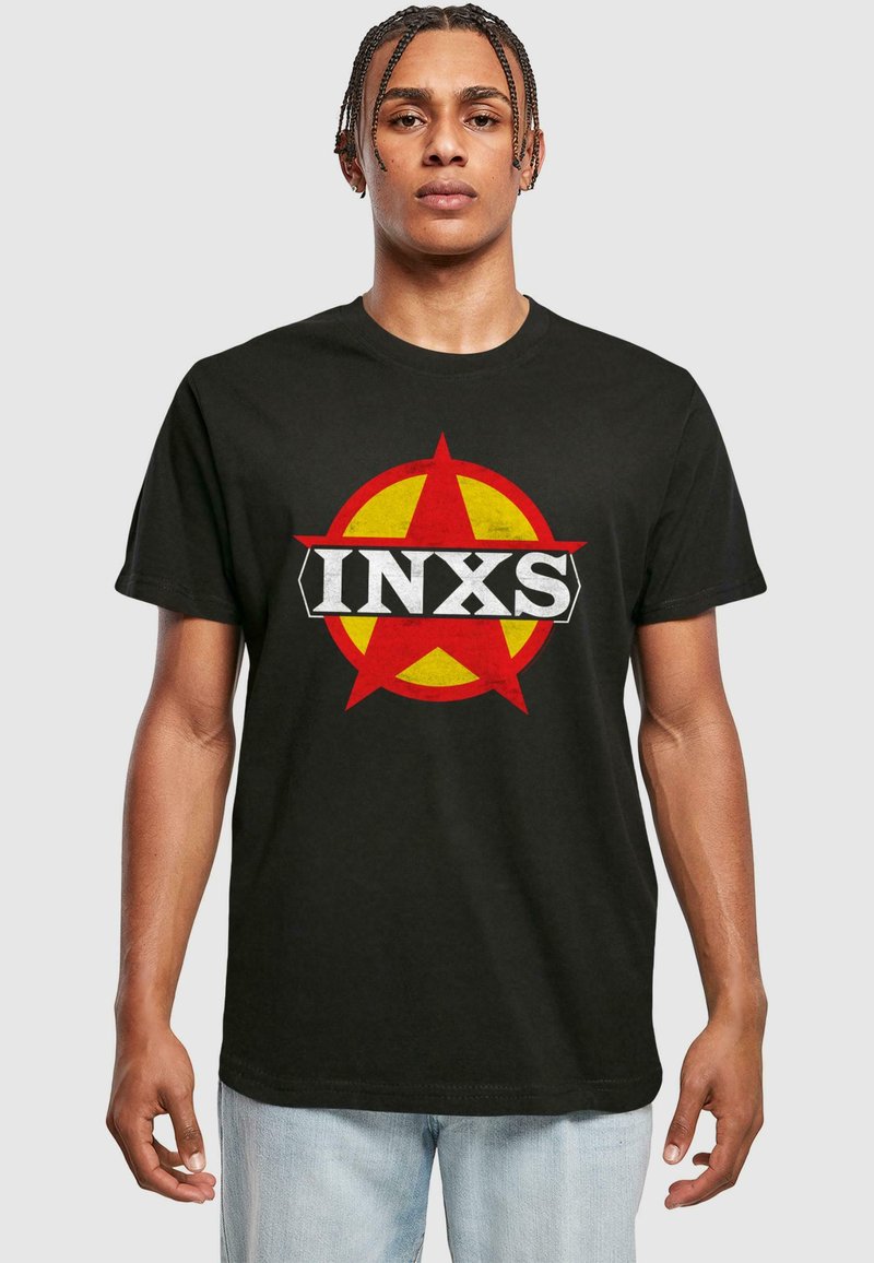 Sort bomulds t-shirt med et rundt rødt og gult logo med en stjerne og teksten "INXS" i fed hvidt på tværs af midten.