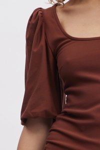 Καφέ εφαρμοστό τοπ με τετράγωνη λαιμόκοψη, με υφασμάτινους φουσκωτούς ώμους και λεία εφαρμογή στο σώμα. Φτιαγμένο από ένα ελαστικό, ελαφρύ ύφασμα.