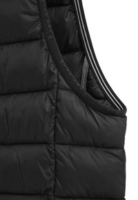 Svart pufferväst med kviltad textur och hög krage. Har ett slätt tyg med tonala sömmar och kontrasterande randiga detaljer vid ärmhålen.