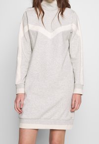 Helles graues Sweatkleid mit hohem Kragen, langen Ärmeln und cremefarbenen Zickzackstreifen über der Vorderseite und an den Ärmeln. Weicher Stoff.