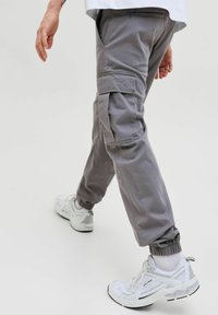 Graue Cargohosen mit elastischen Bündchen, Seitentaschen und lockerem Sitz, kombiniert mit weißen Sneakers mit grauen Akzenten und Schnürsenkeln.