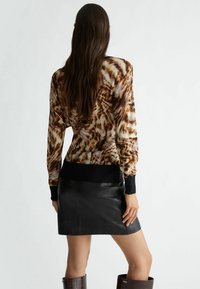 Pullover marrone e crema a tie-dye con maniche lunghe e polsini a coste neri, abbinato a una mini gonna in pelle nera, elegante e aderente.