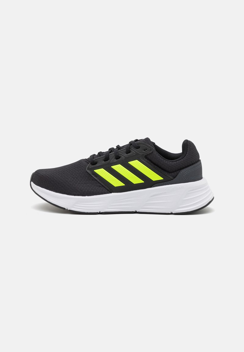 Chaussure de sport noire avec une tige en mesh, présentant trois bandes réfléchissantes jaune fluo, une semelle intermédiaire blanche rembourrée et un talon renforcé.