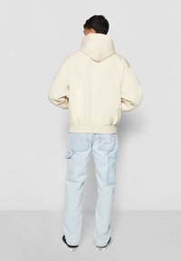 Beige hettegenser med løs passform, ribbede mansjetter og hem. Kombinert med lyseblå cargo-bukser med sidelommer og logodetaljer.