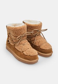 Stivali foderati in pelliccia color sabbia con un esterno testurizzato, dettagli in suede, laccio decorativo e una suola in gomma spessa per comfort e durata.