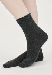 Grå ullstrumpor med ribbad mudd och texturerad yta som visas på ett ben. Har en liten tygetikett bak.