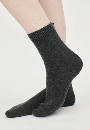 Graue Wollsocken mit einem gerippten Bündchen und strukturierter Optik, die an einem Bein gezeigt werden. Sie verfügen über ein kleines Stoffetikett auf der Rückseite.