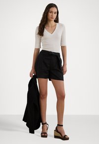 Body bianco con scollo a V e maniche a tre quarti abbinato a pantaloni corti neri a vita alta con cintura. Sandali neri con zeppa e cinturino alla caviglia.