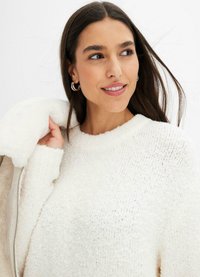 Maglione bianco in tessuto con scollo rotondo, caratterizzato da una finitura pelosa e maniche lunghe, abbinato a un cappotto di colore chiaro.