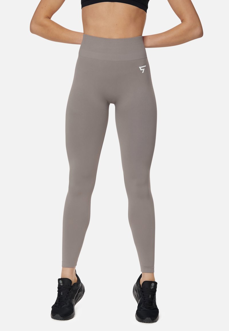 Leggings a vita alta in taupe, realizzati in tessuto elasticizzato. Presentano una texture liscia e un dettaglio con logo bianco sulla vita.