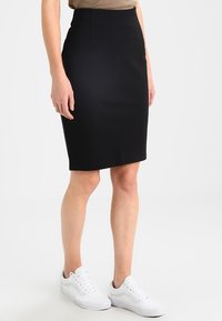 Black pencil skirt with a high waist and smooth texture, paired with white sneakers for a casual look. Skirt has a fitted silhouette.