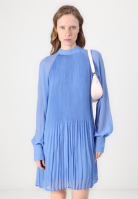 Light blue pleated dress with long sleeves and a high neckline, made of soft fabric. Accompanied by a small pink handbag on the shoulder.