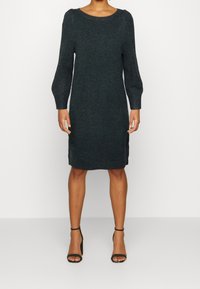 Mörkgrön stickad klänning med rundad halsringning, långa puffärmar och rak siluett. Har en knälång längd och texturerad tyg.