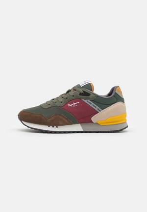 Green sneaker with brown suede accents, maroon mesh panel, gray heel, and yellow sole; features lace-up design and padded tongue.