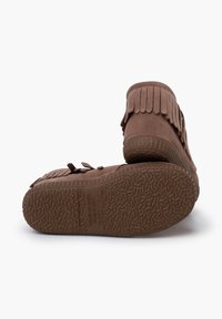 Bruine suede moccasin-stijl schoenen met franjes, een flexibele rubberen zool met een gestructureerd grippatroon en decoratieve strikken aan de zijkanten.