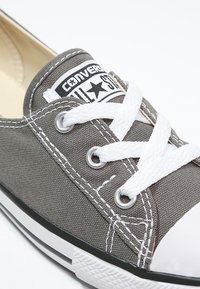 Sneaker in tela grigia con lacci bianchi, punta in gomma e patch logo nero. Presenta cuciture bianche e occhielli in metallo.