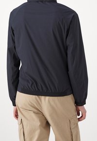 Navy lightweight jacket with elastic cuffs and hem, featuring a simple design. Material appears smooth with a matte finish, suitable for casual wear.