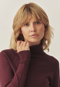 Pulover midi burgund cu guler înalt, fabricat dintr-un material tricotat cu caneluri, cu mâneci lungi și un design ajustat. Textură netedă cu detalii subtile.