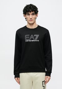 Fekete, hosszú ujjú pulóver kerek nyakkal, fehér EA7 és Emporio Armani logókkal. Az anyag simának tűnik; bordázott mandzsetták és szegély.