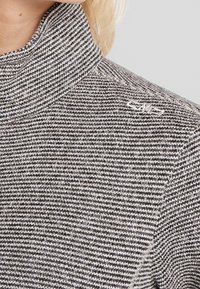 Suéter a rayas grises y blancas con cuello alto, presenta un tejido texturizado y un pequeño logo bordado en el hombro.